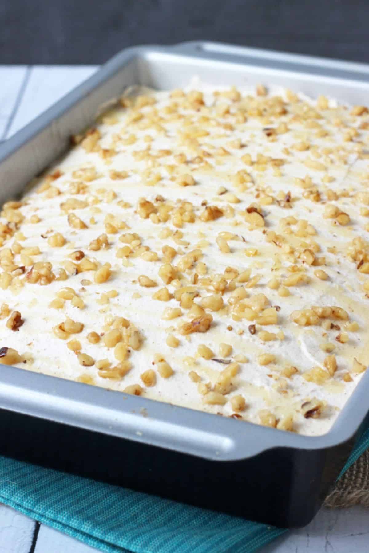 Baklava poke cake in a metal baking pan on a dark teal napkin.