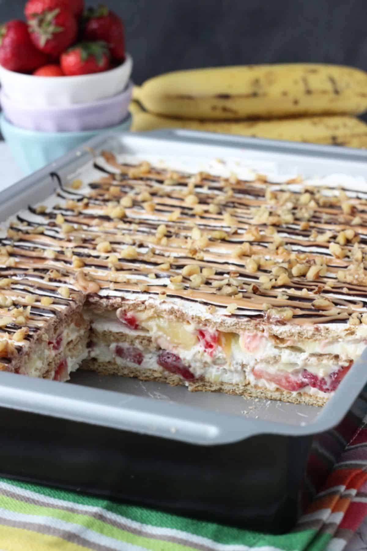 A banana split icebox cake in a metal baking pan with a few slices removed to show layers.
