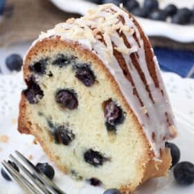 A slice of blueberry coconut bundt cake on a white plate next to a fork.