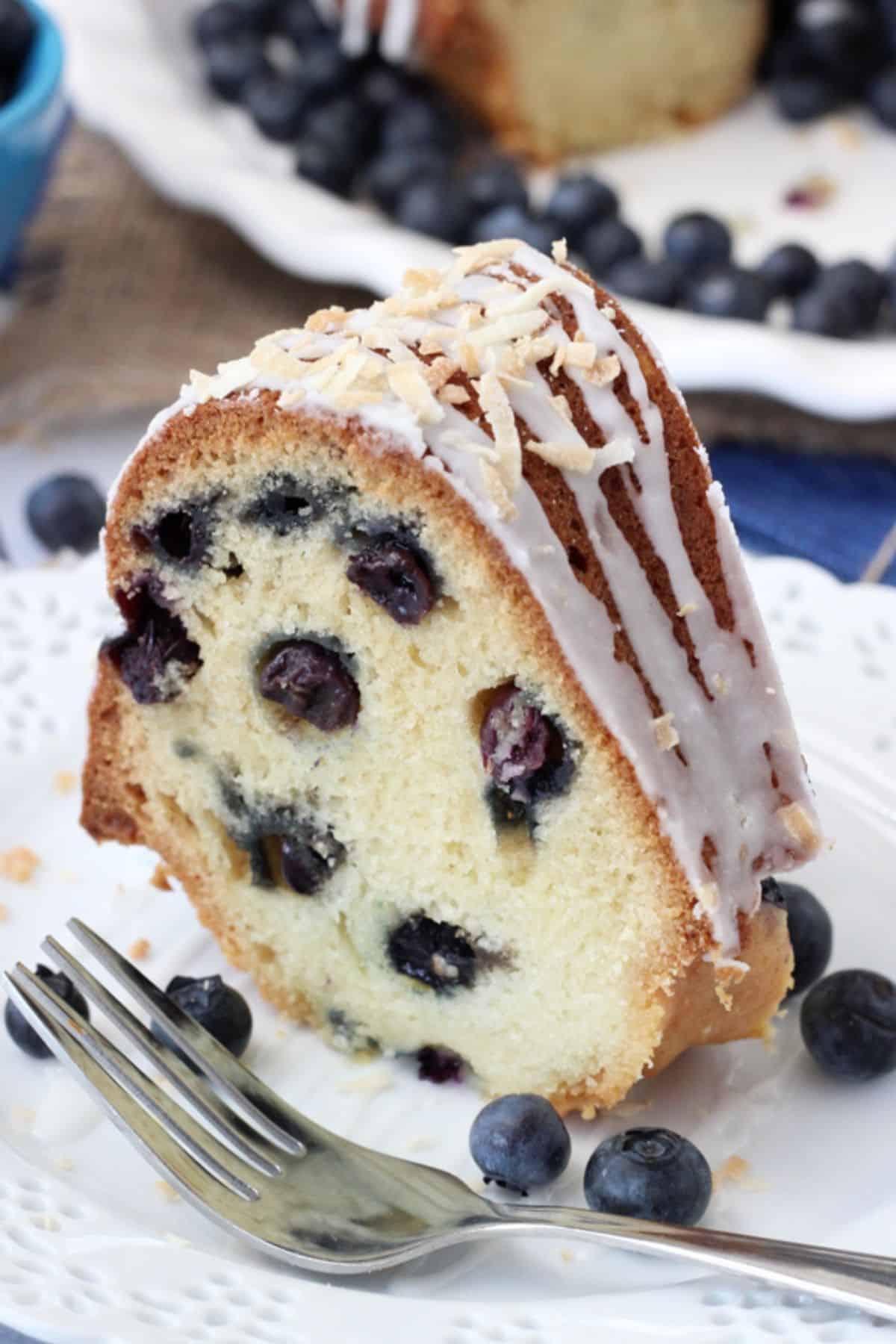 A slice of blueberry coconut bundt cake on a white plate next to a fork.