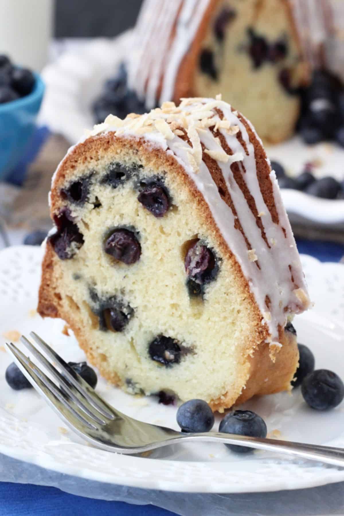 Close up of a slice of blueberry coconut bundt cake on a white plate next to a fork.