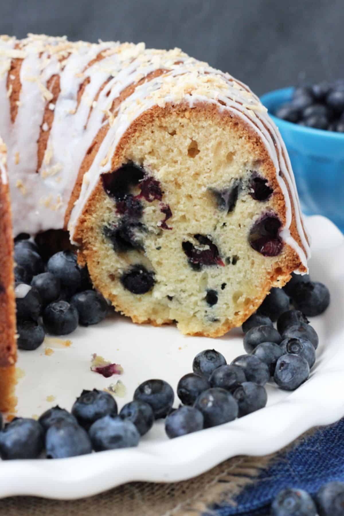 A blueberry coconut bundt cake on a white cake plate with a few slices removed to see inside.