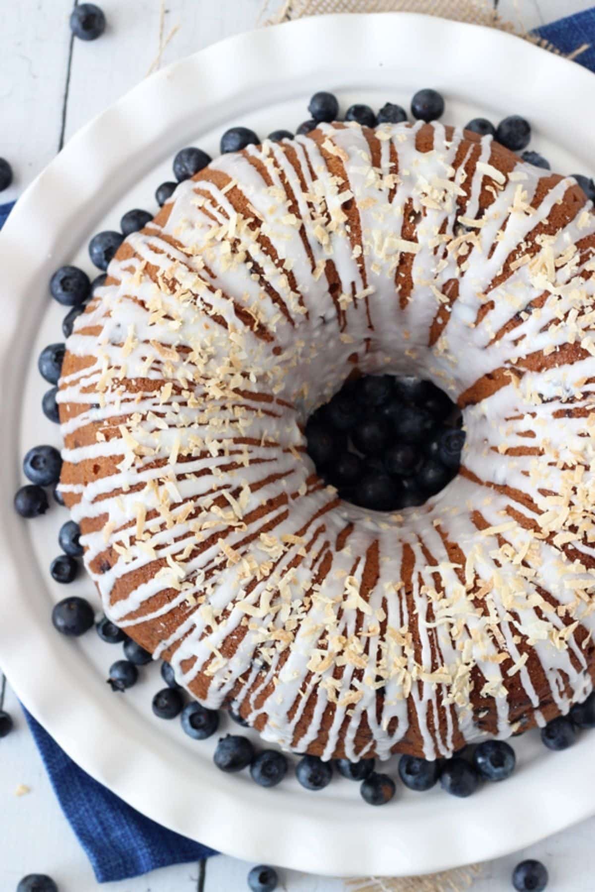 Overhead view of a blueberry coconut bundt cake on a white cake plate surrounded by blueberries.