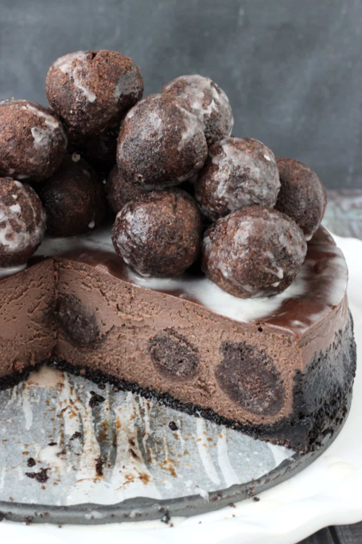 A chocolate donut hole cheesecake piled with donut holes with a few slices removed to show inside.