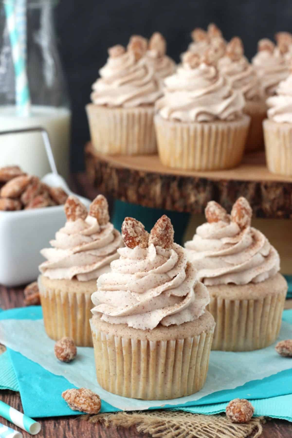 Three cinnamon sugar almond cupcakes on a teal napkin with more cupcakes in the background.