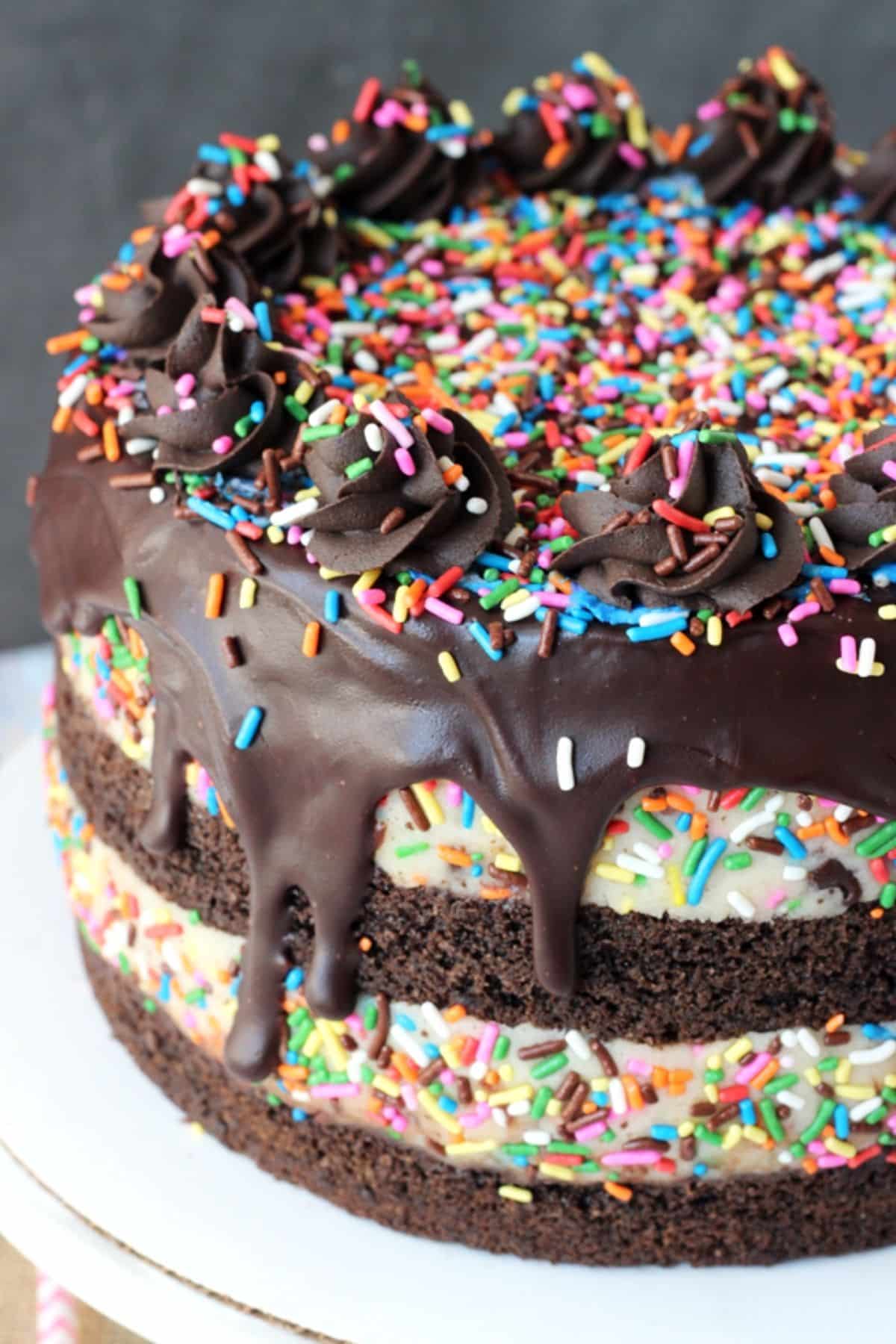 Close up of a cookie dough brownie layer cake on a white cake plate.