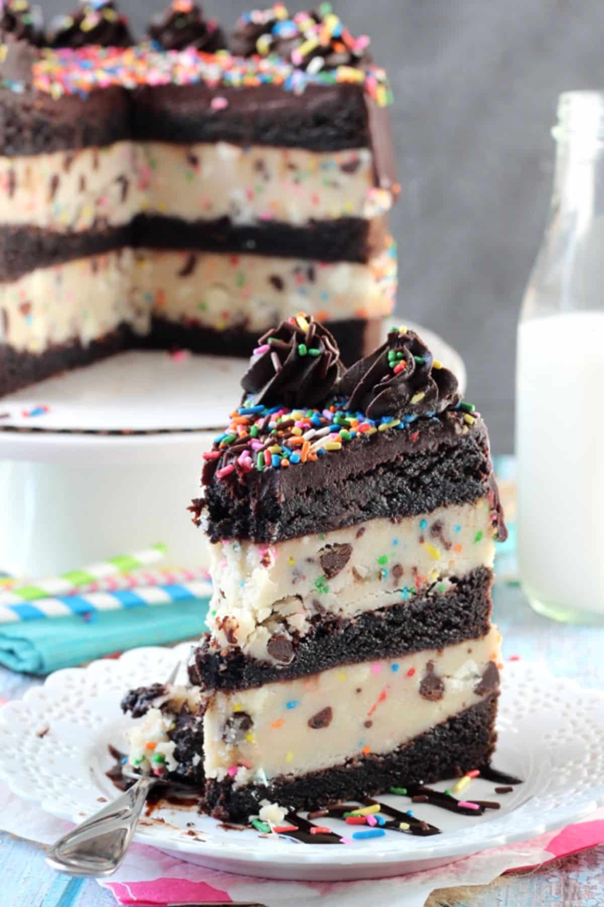 A slice of cookie dough brownie layer cake with a bite removed to show layers with the rest of the cake in the background.