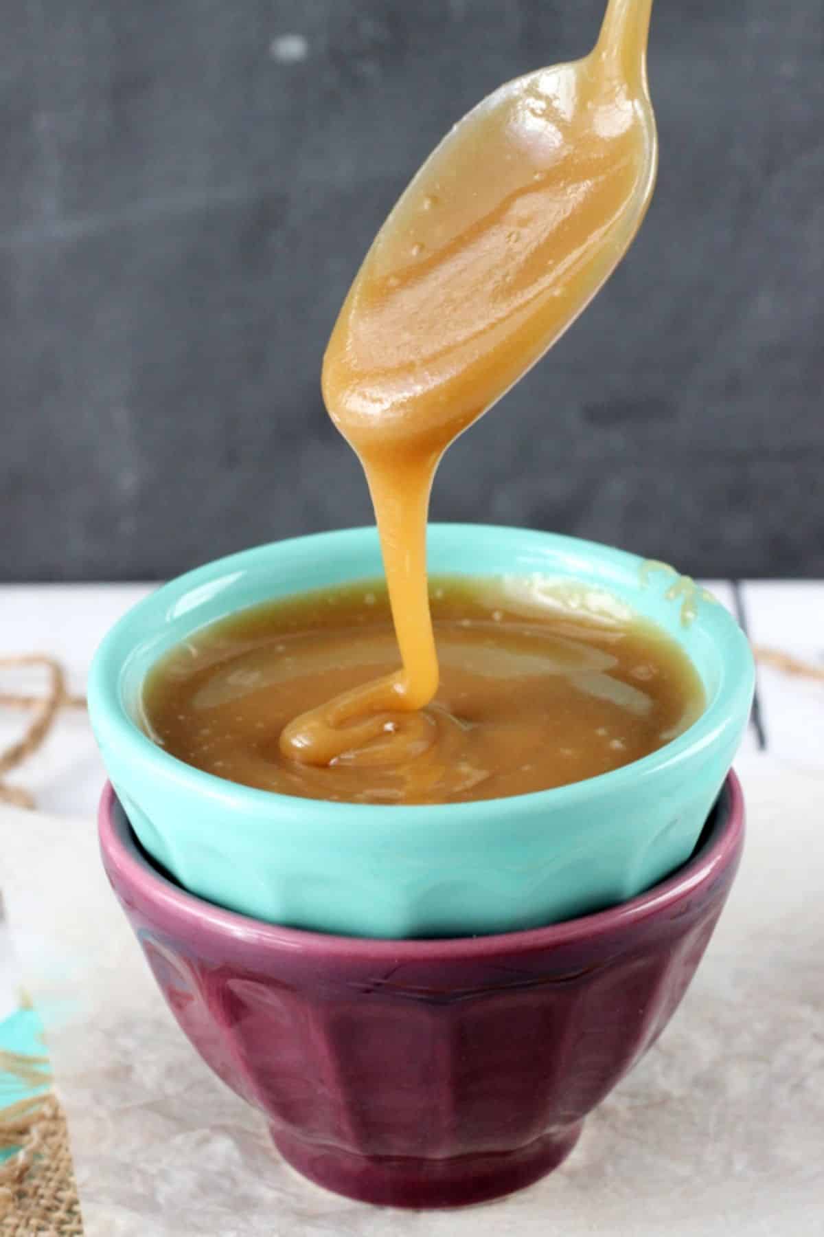 A teal bowl filled with caramel with a spoon above dripping caramel into the bowl.