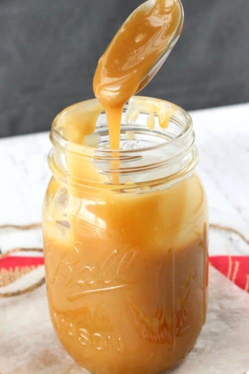 A spoon covered with caramel dripping back into a jar of caramel.