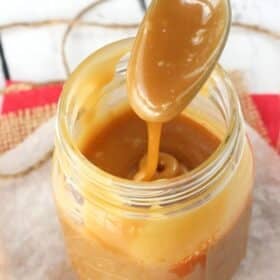 A spoon dripping caramel back into a jar of more caramel.