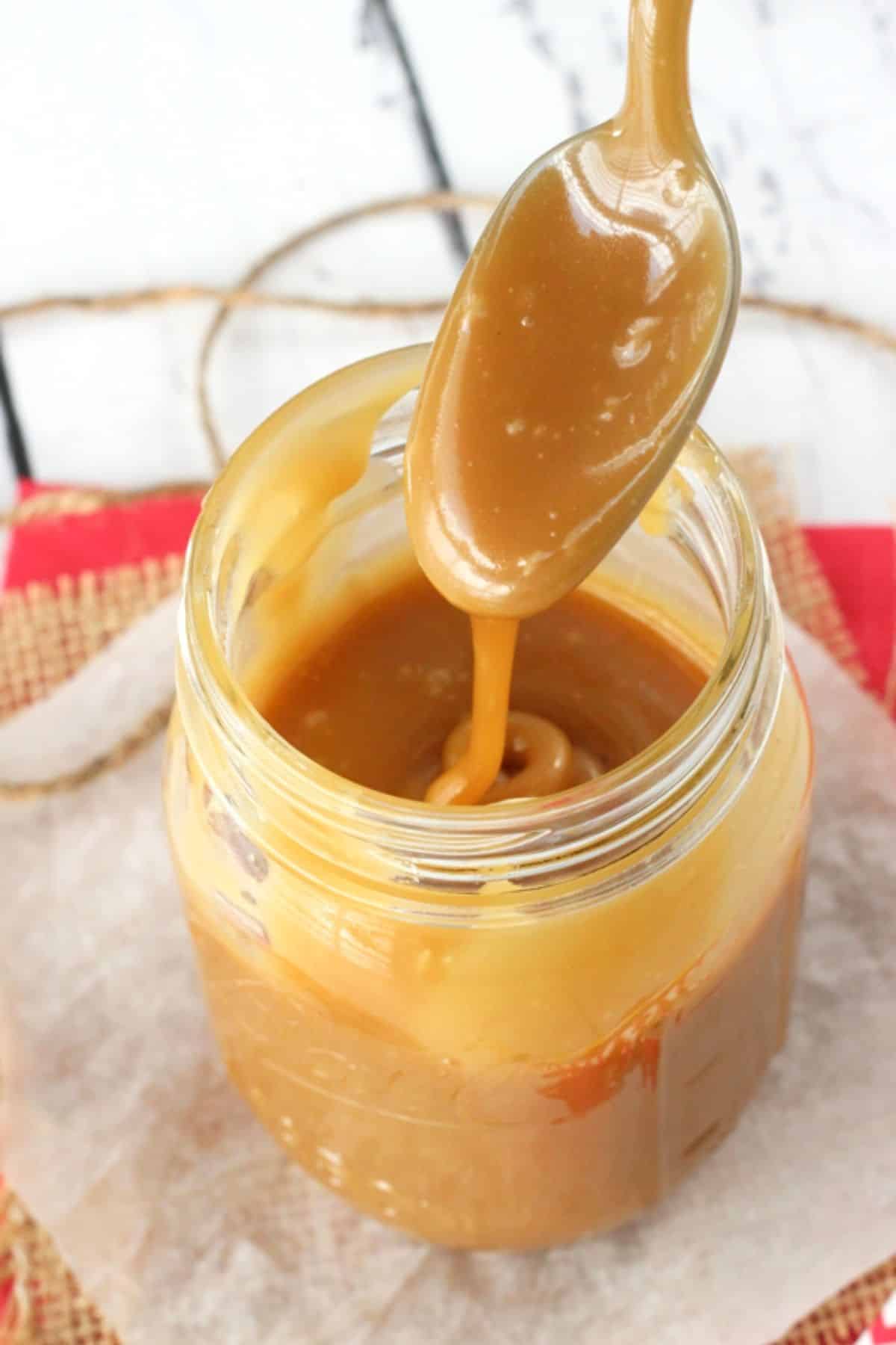 A spoon dripping caramel back into a jar of more caramel.