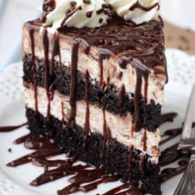 Close up of a tall slice of hot fudge swirl ice cream cake on a small white plate.
