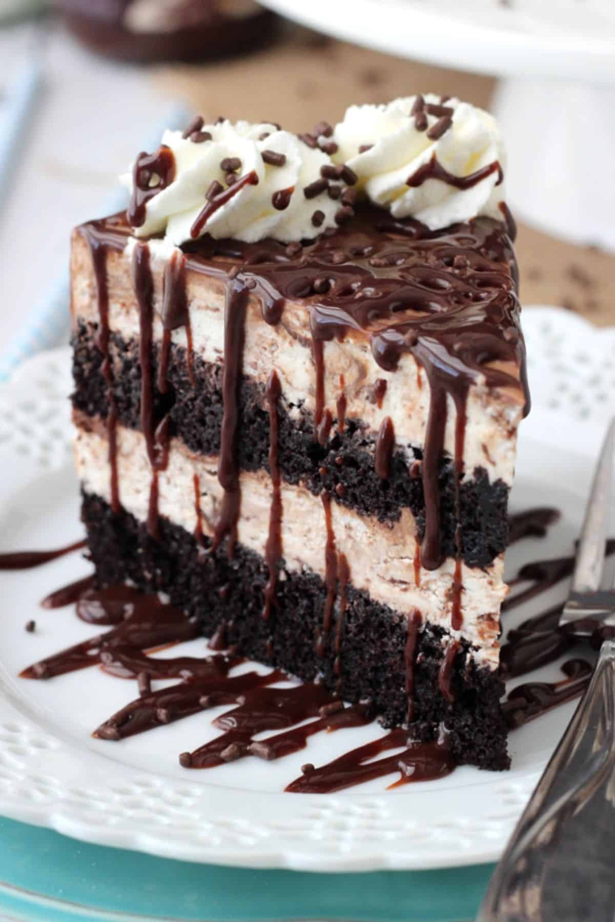 Close up of a tall slice of hot fudge swirl ice cream cake on a small white plate.