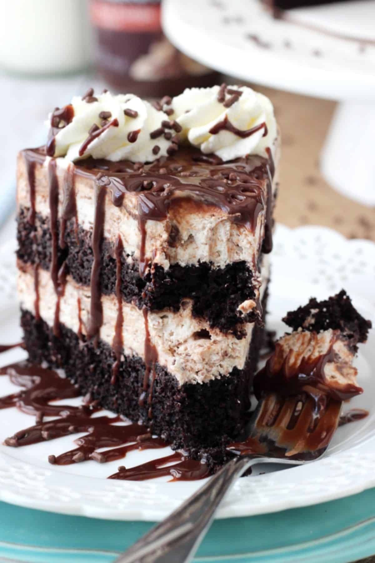 A tall slice of hot fudge swirl ice cream cake with a bite removed on a fork.