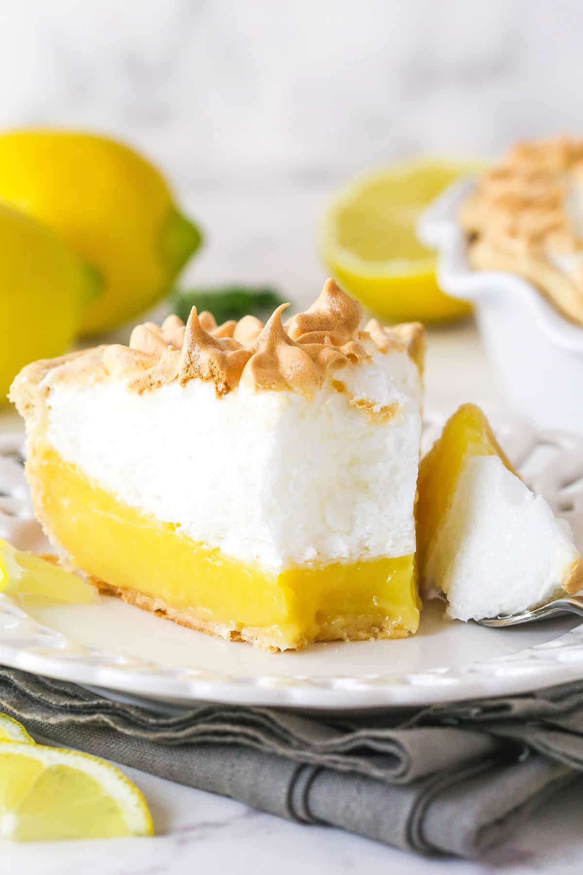 This classic lemon meringue pie features a tart lemon filling in a buttery crust topped with a light but stable meringue. Front view of a slice of lemon meringue pie on a plate with a bite on a fork