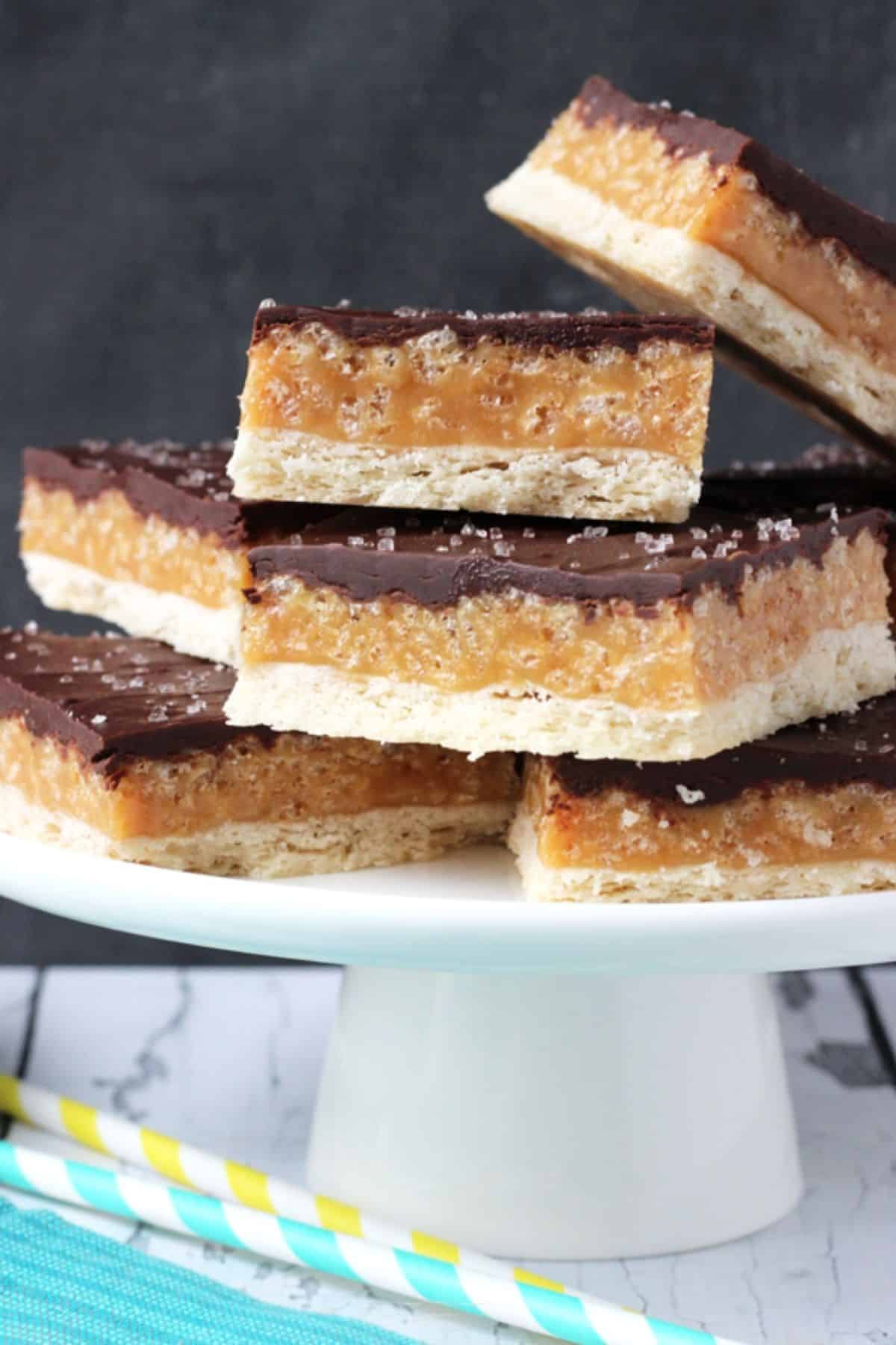 A white cake stand topped with caramel shortbread bars.