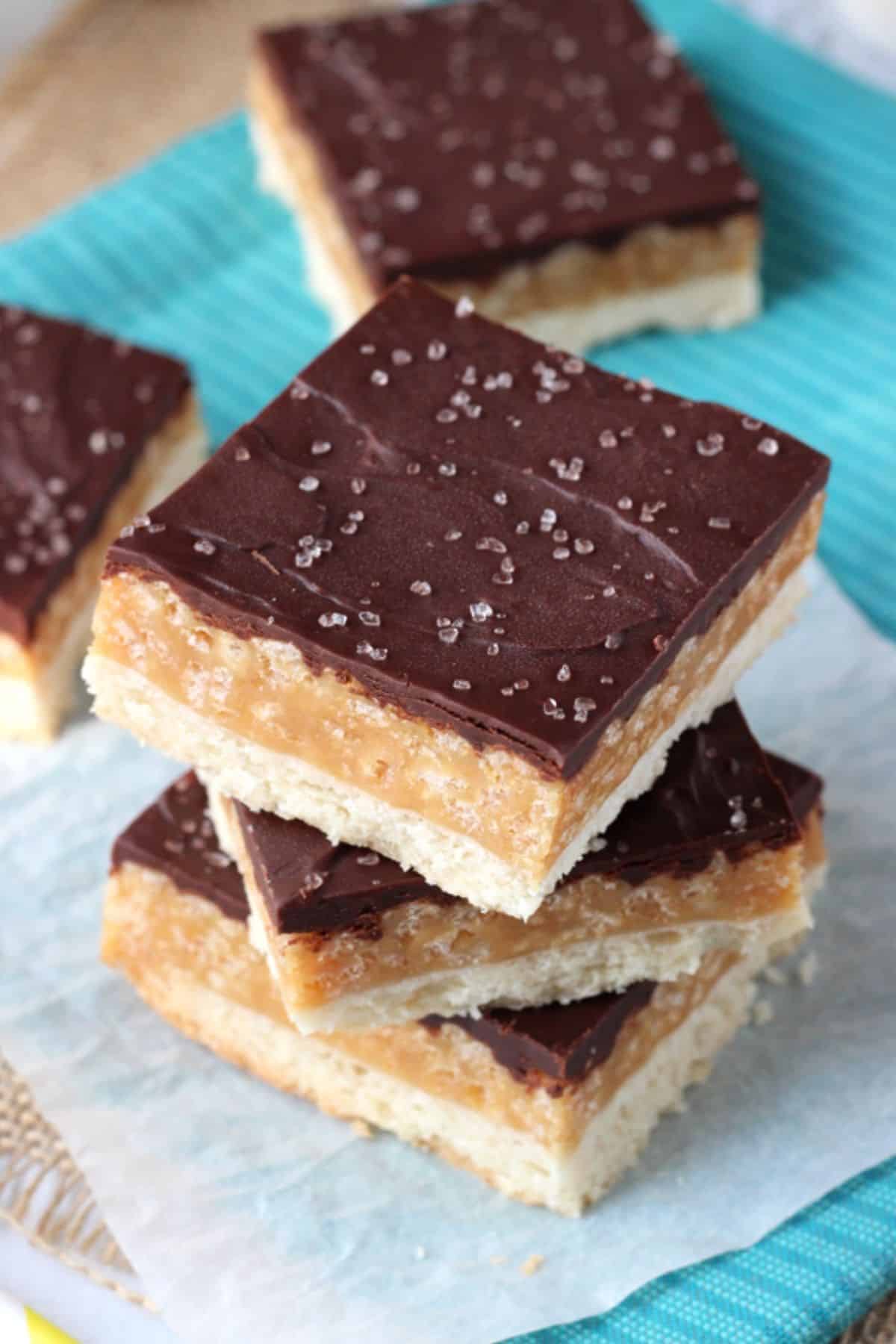 Top view of a stack of three caramel shortbread bars on a piece of parchment.