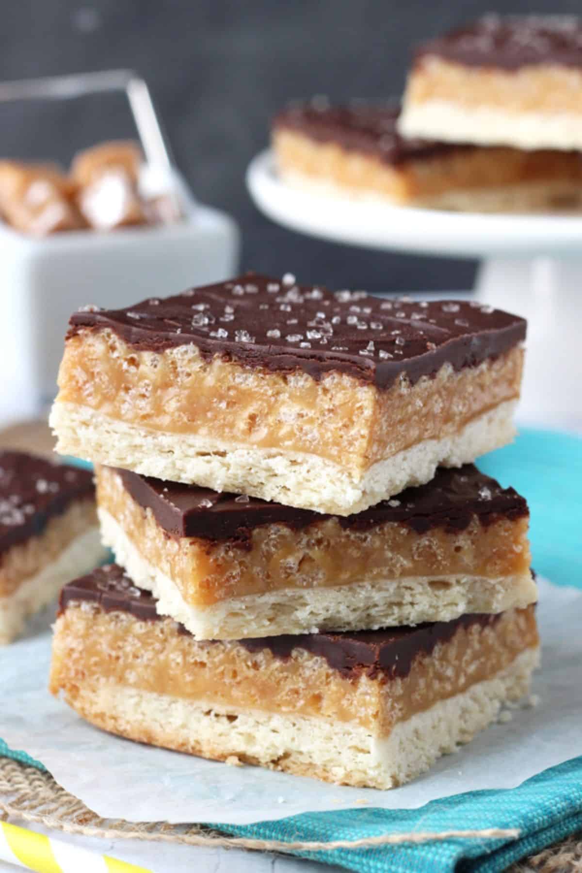 A stack of three caramel shortbread bars on a teal napkin.