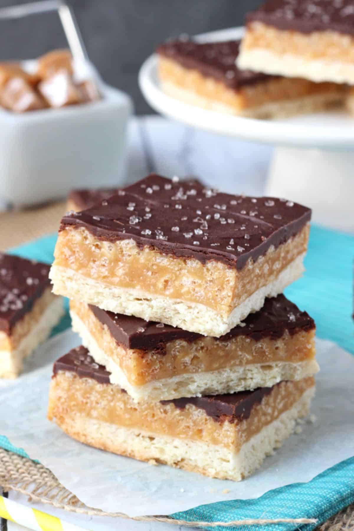 A stack of three caramel shortbread bars on a teal napkin.