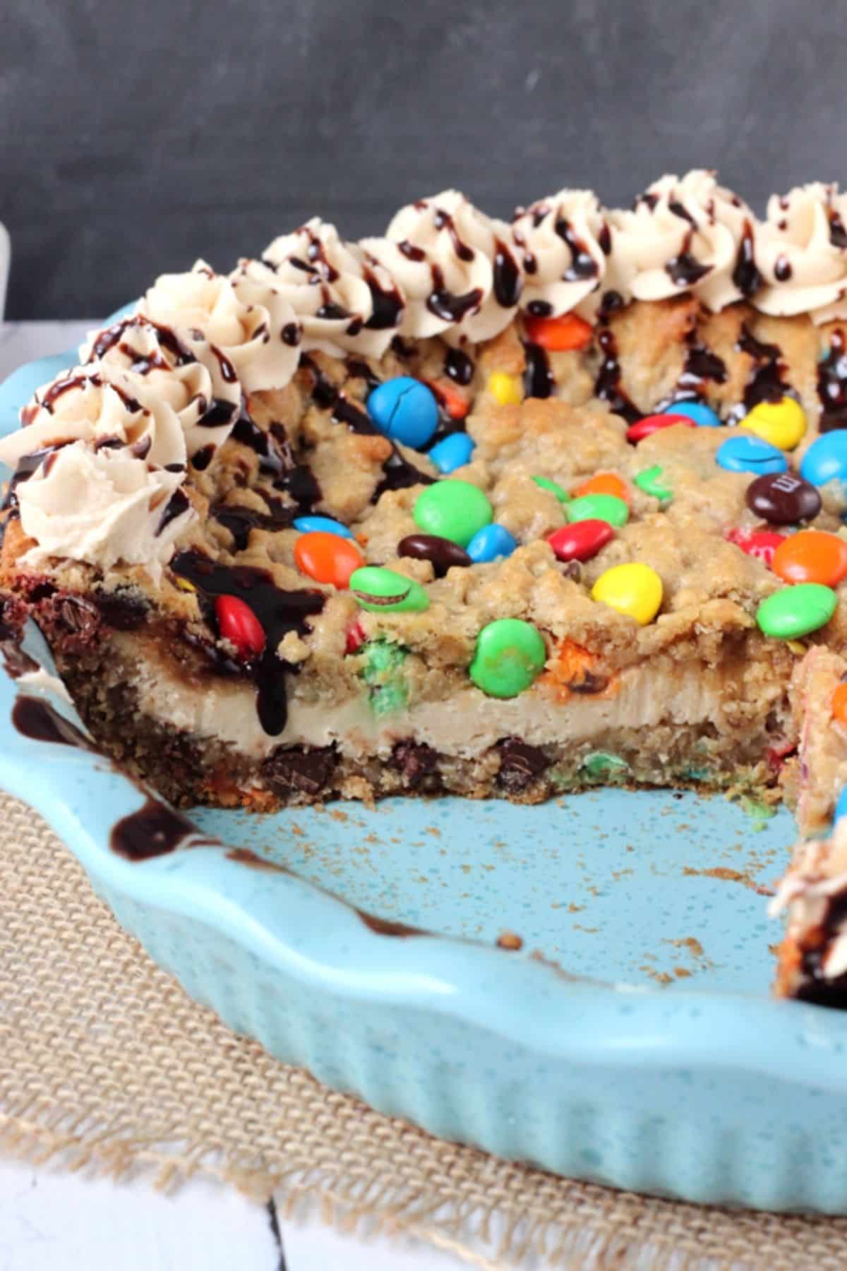 A monster cookie cheesecake pie in a blue pie pan with a few slices removed to show internal layers.