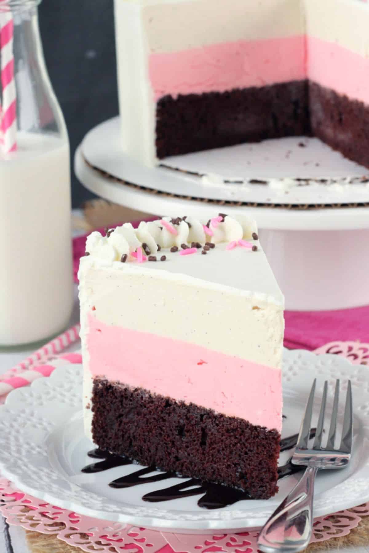 Close up of a slice of neapolitan ice cream cake with the rest of the cake in the background.