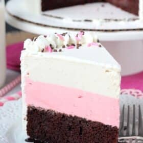 Close up of a slice of neapolitan ice cream cake with the rest of the cake in the background.
