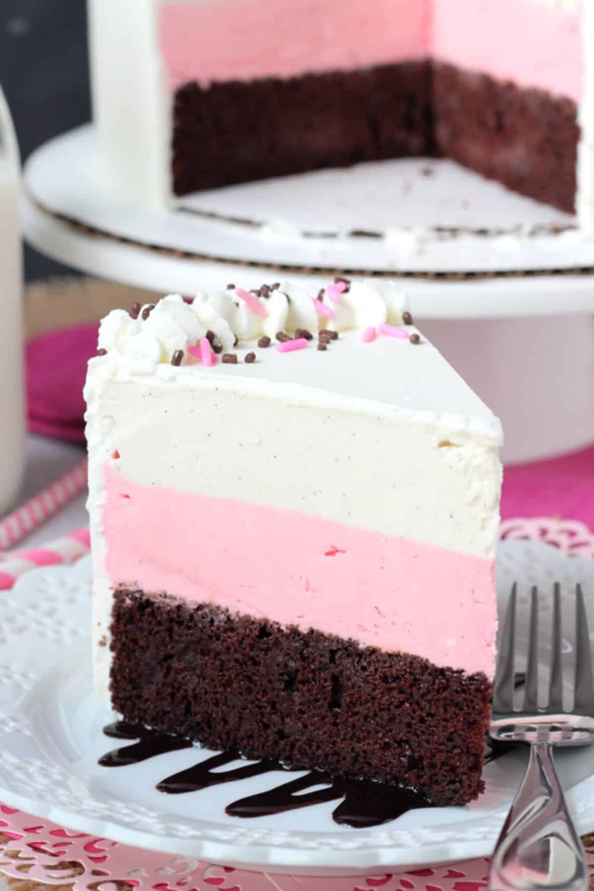 Close up of a slice of neapolitan ice cream cake with the rest of the cake in the background.