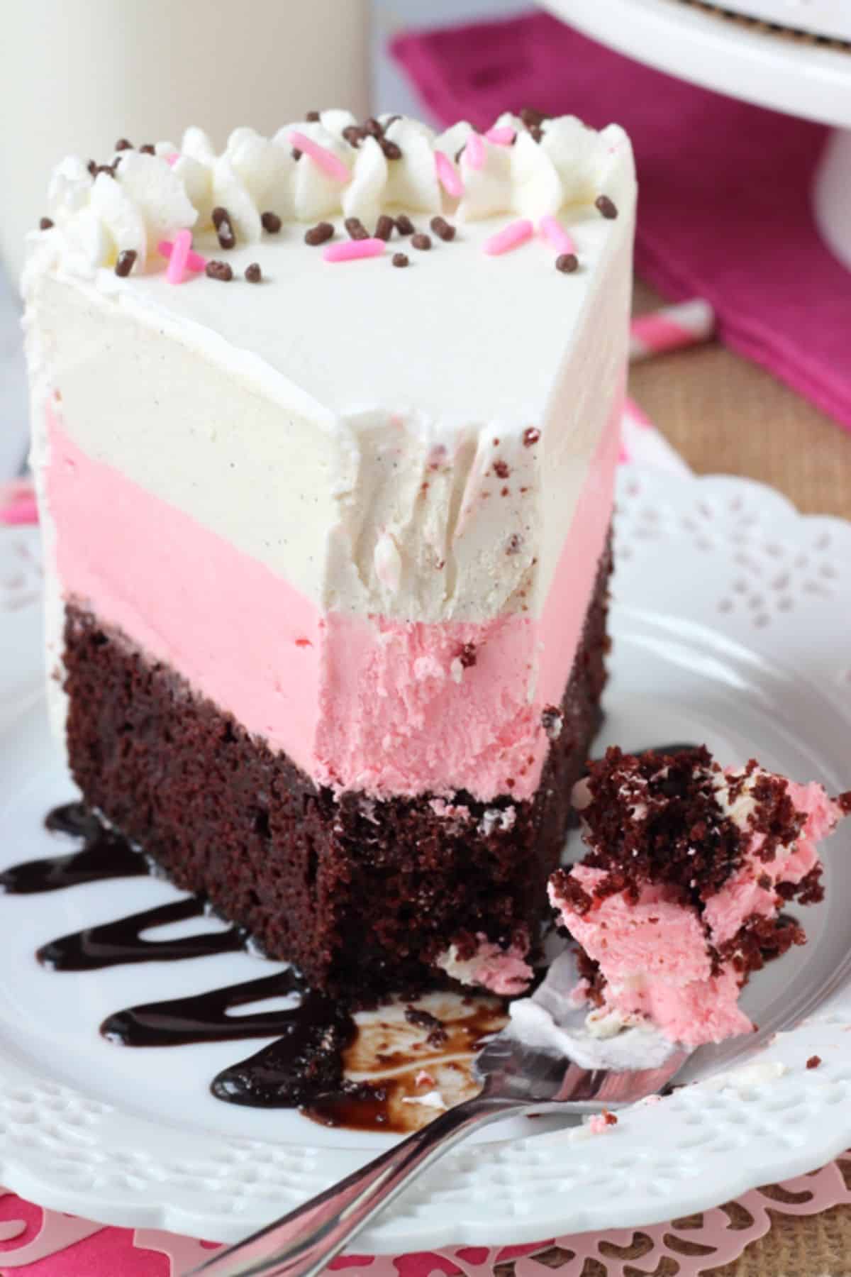 A tall slice of neapolitan ice cream cake with a bite removed on a fork.
