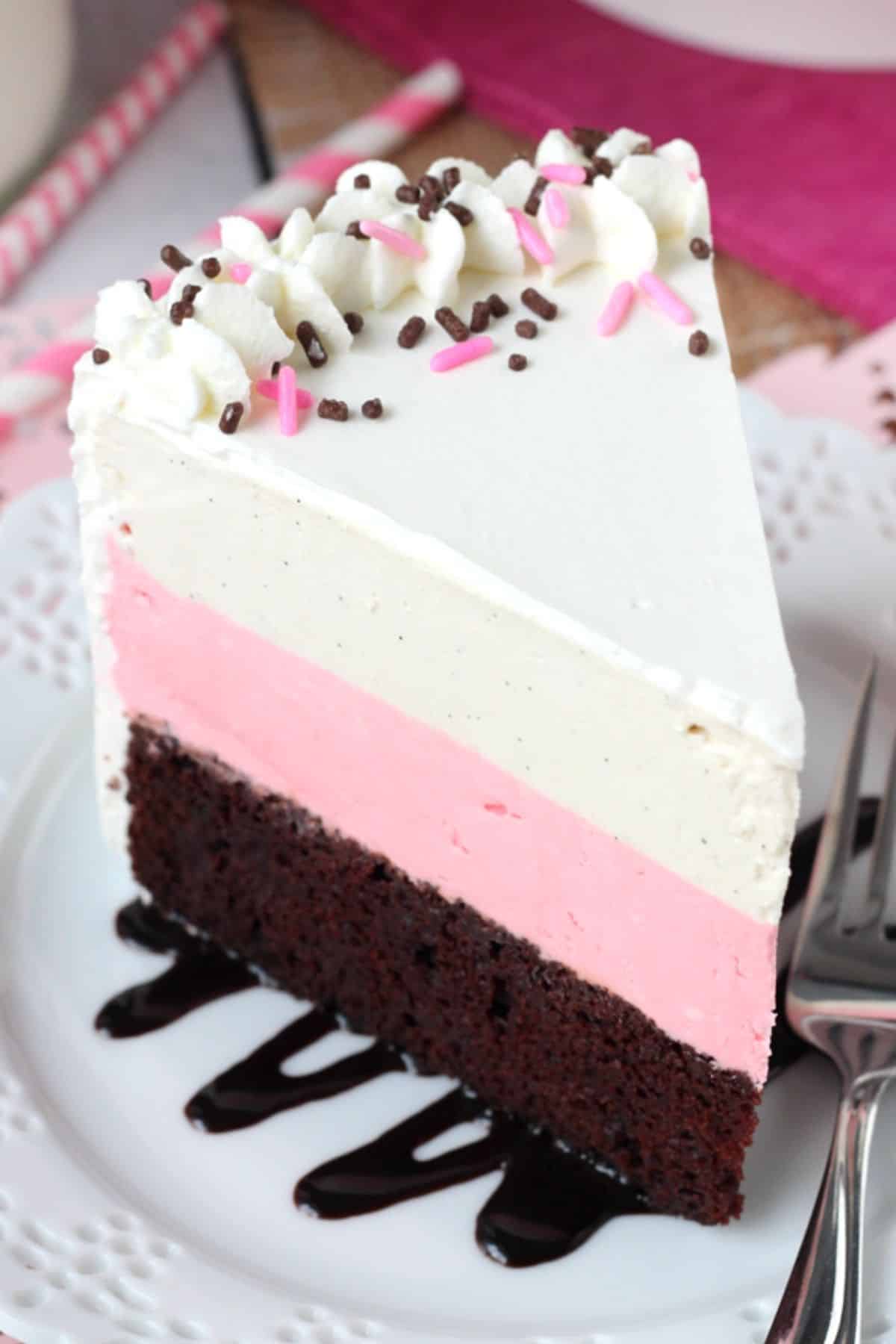 A tall slice of neapolitan ice cream cake on a small white plate.