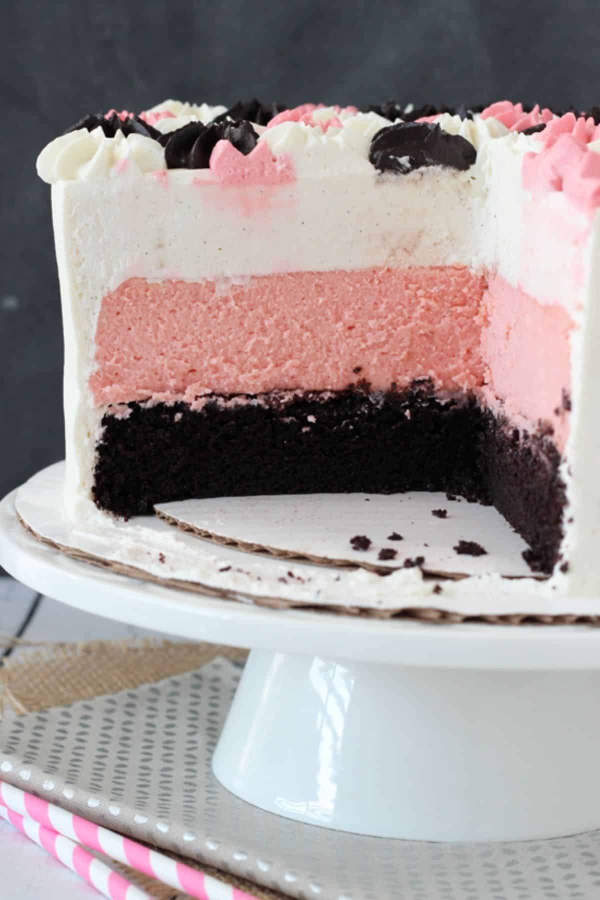 A neapolitan millionaire cake on a white cake stand with slices removed to show layers.