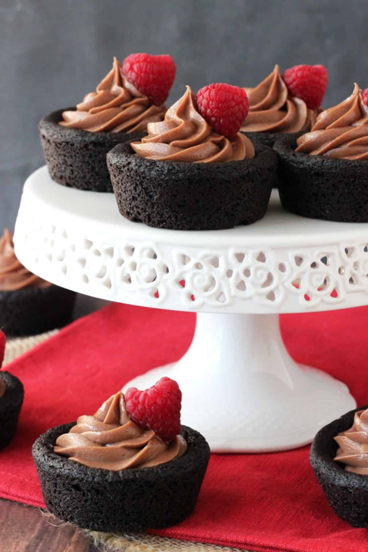 Close up of a few Nutella cheesecake chocolate cookie cups on top of a white cake stand with more below the stand.
