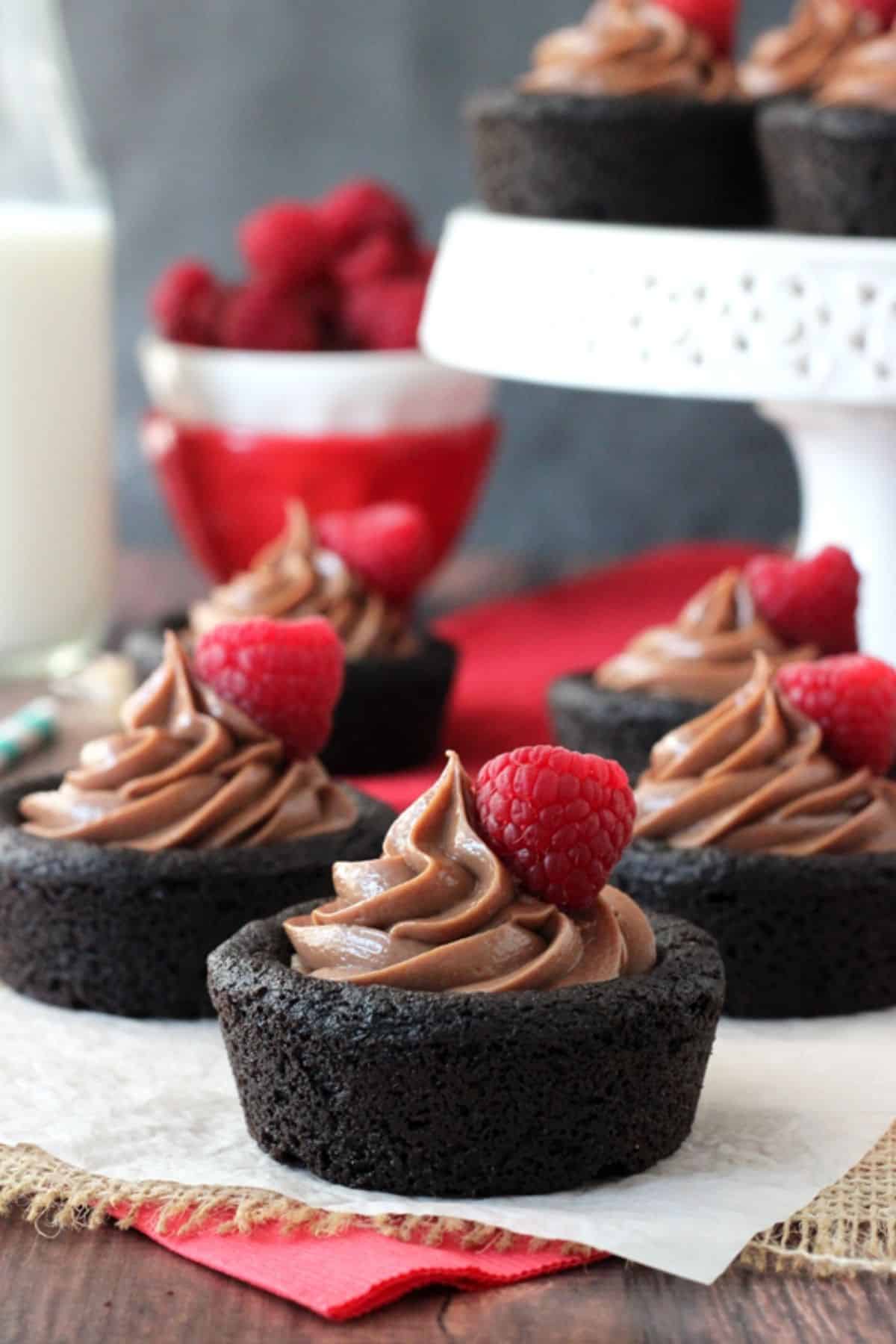 Several Nutella cheesecake chocolate cookie cups on a piece of parchment with more cups in the background.