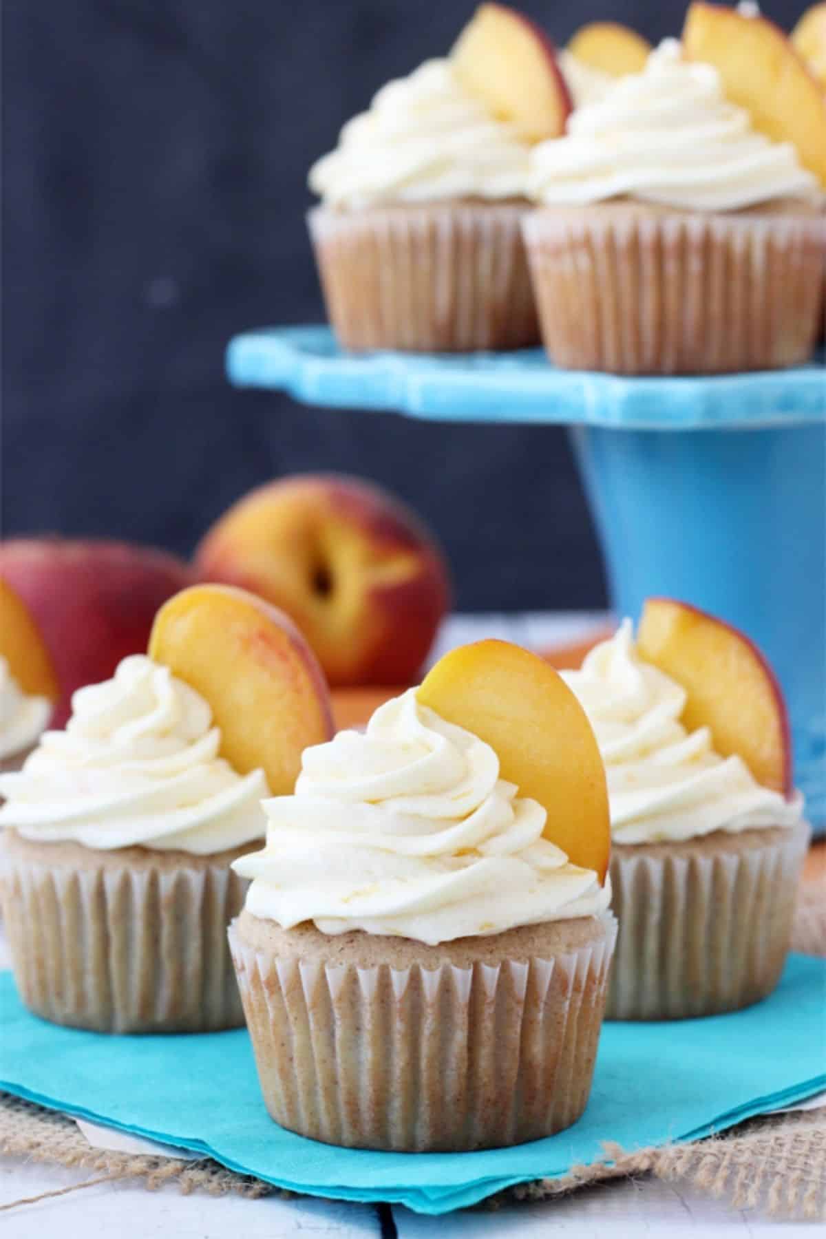 Three peach pie cupcakes on a teal napkin with more cupcakes in the background on a blue cake stand.