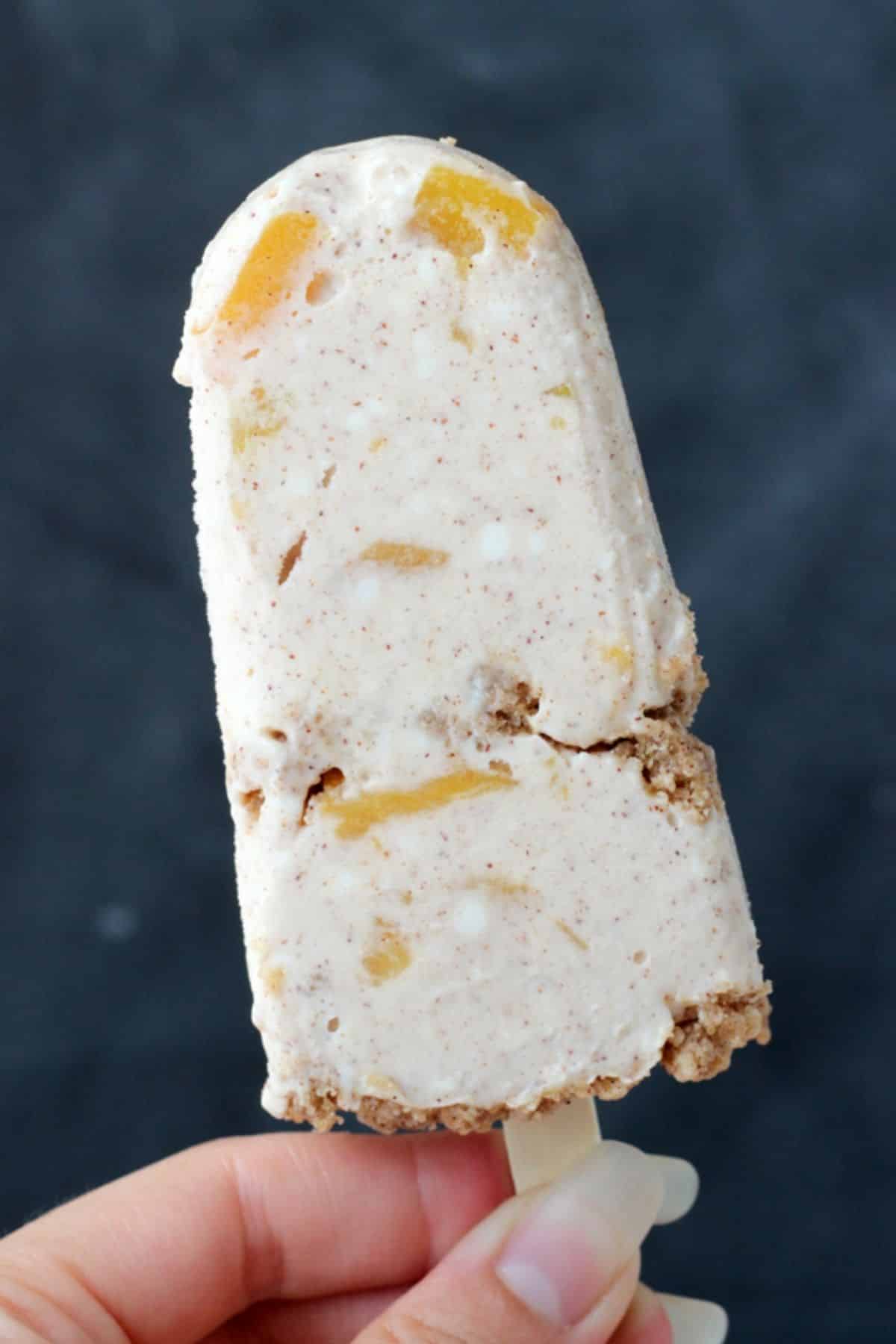 A hand holding up a peach streusel popsicle.