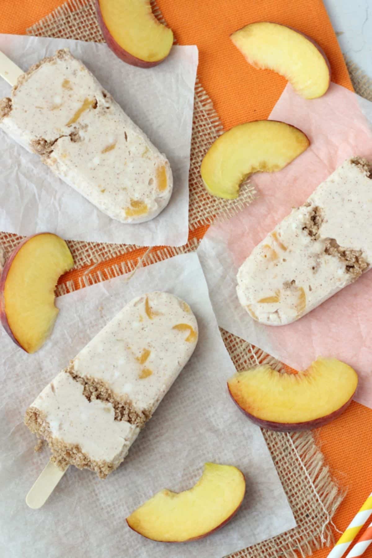3 peach streusel popsicles laying on parchment next to peach slices.