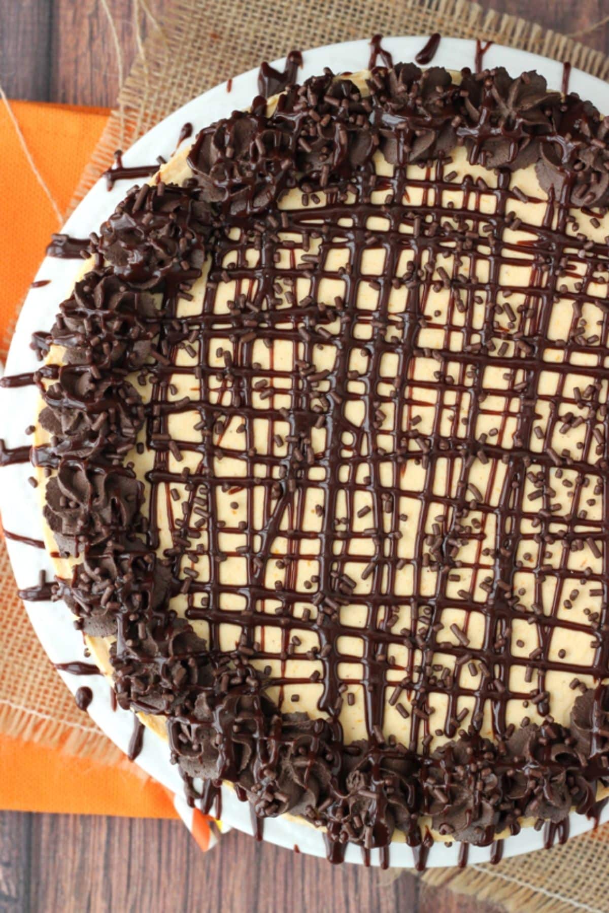 Top view of a pumpkin chocolate brownie cheesecake drizzled with chocolate on a white cake plate.