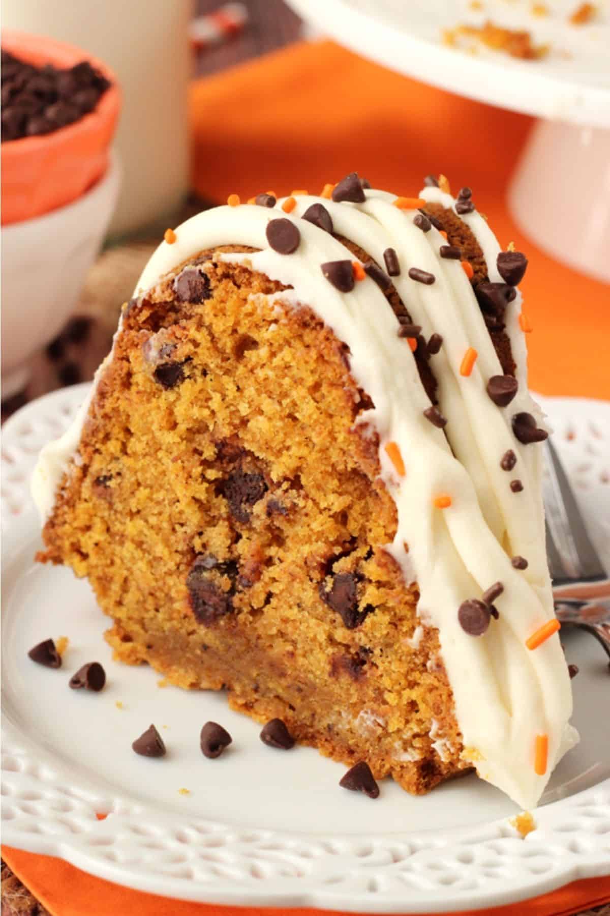 This pumpkin bundt cake with chocolate chips is soft, moist, and full of fall spices and gooey chocolate. It's perfect for Thanksgiving! Close up of a slice of pumpkin chocolate chip bundt cake on a small white plate.
