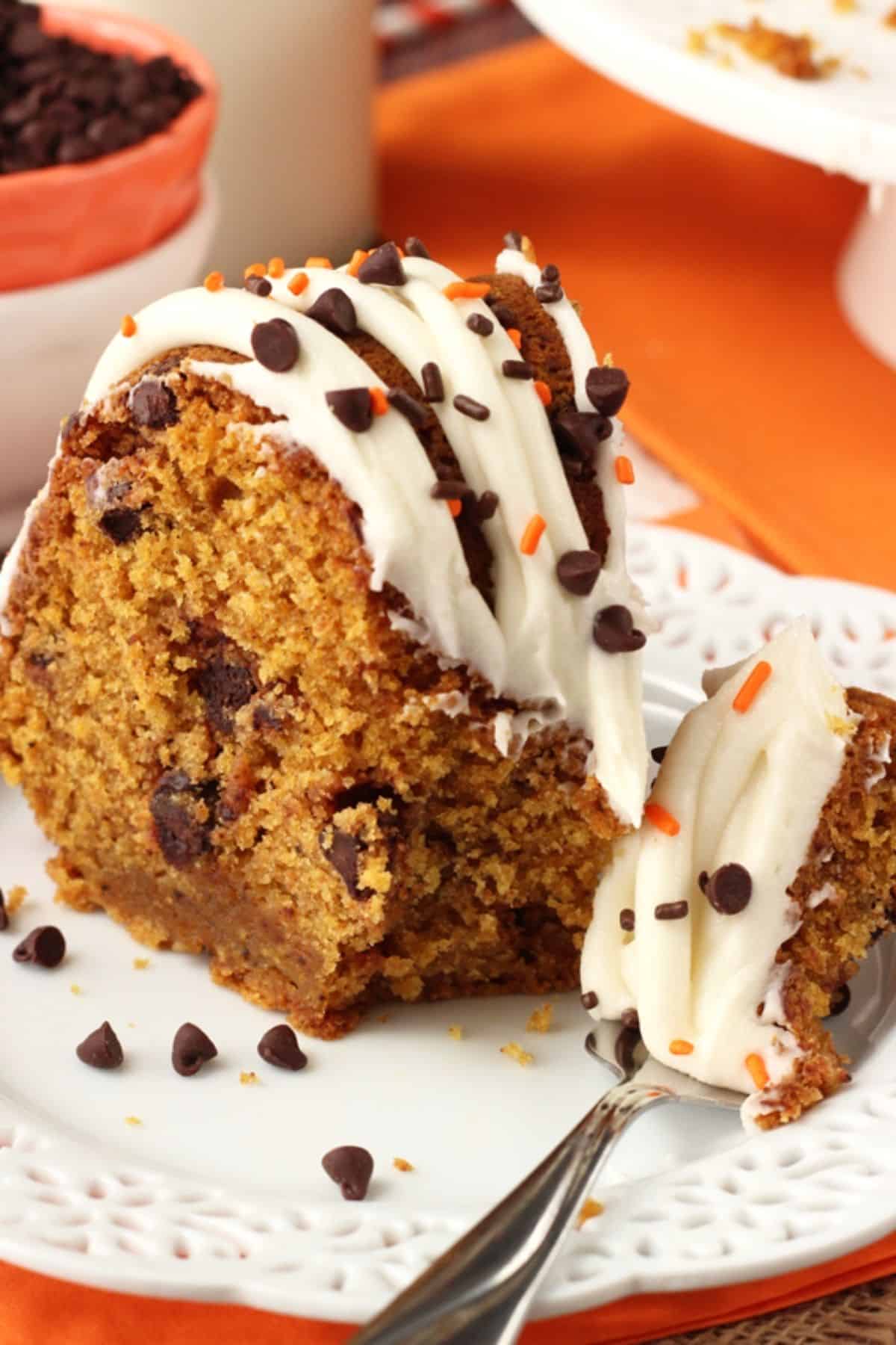 This pumpkin bundt cake with chocolate chips is soft, moist, and full of fall spices and gooey chocolate. It's perfect for Thanksgiving! Close up of a slice of pumpkin chocolate chip bundt cake with a bite removed on a fork.