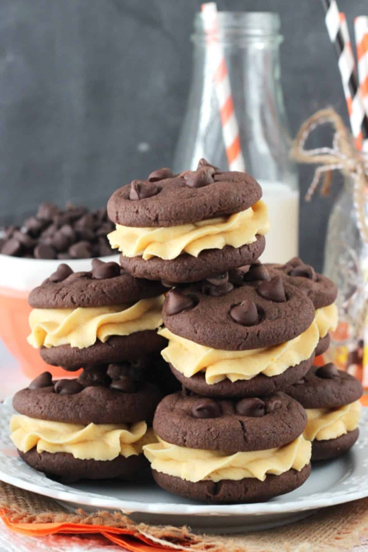 Pumpkin Chocolate Chip Cookie Sandwiches A pile of pumpkin chocolate chip cookie sandwiches on a white plate with milk in the background.