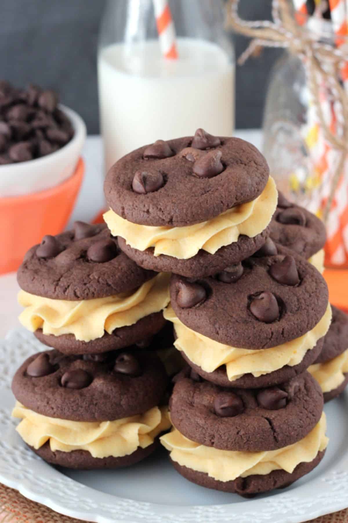 Pumpkin Chocolate Chip Cookie Sandwiches A pile of pumpkin chocolate chip cookie sandwiches on a white plate with milk in the background.