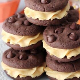 Close up of a pile of pumpkin chocolate chip cookie sandwiches on a white plate.