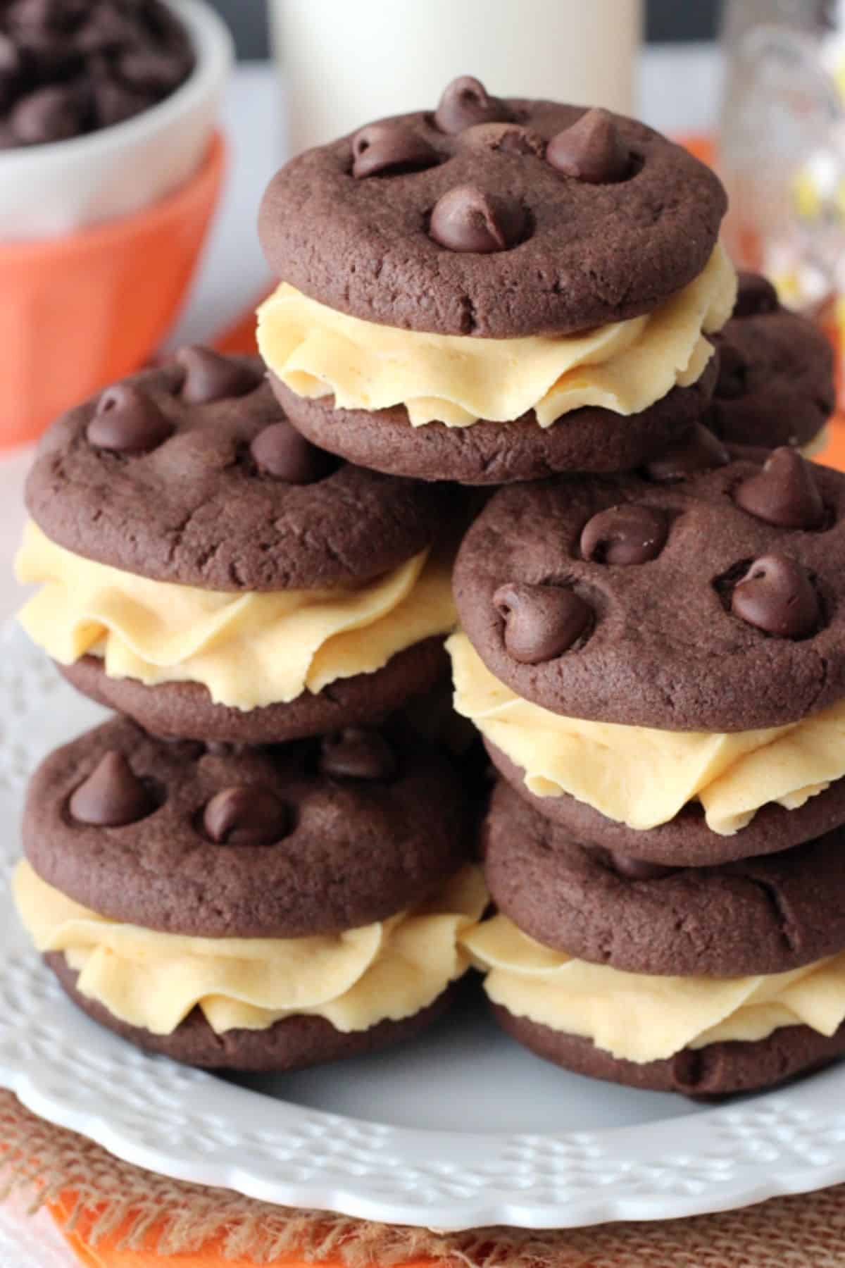 Close up of a pile of pumpkin chocolate chip cookie sandwiches on a white plate.