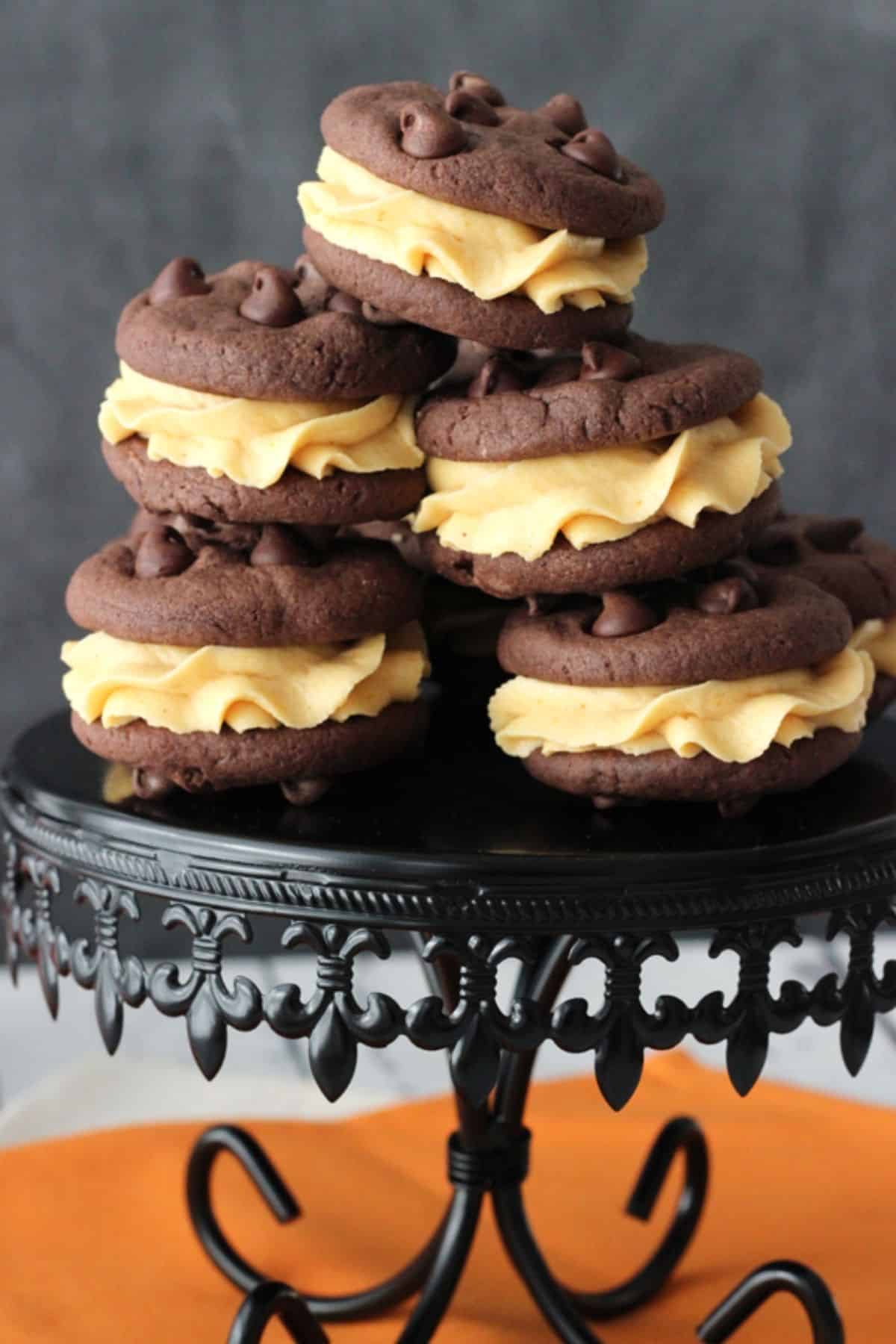 Pumpkin Chocolate Chip Cookie Sandwiches A stack of pumpkin chocolate chip cookie sandwiches on an ornate black cake stand.