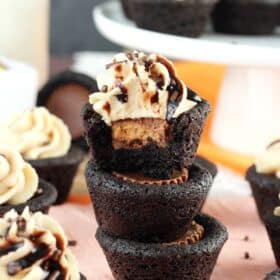 A stack of 3 Reese's chocolate cookie cups with a bite taken out of the top cookie.