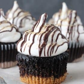 Close up of a S'mores Cupcake on a piece of parchment with more cupcakes in the background.