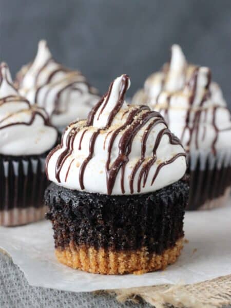Close up of a S'mores Cupcake on a piece of parchment with more cupcakes in the background.