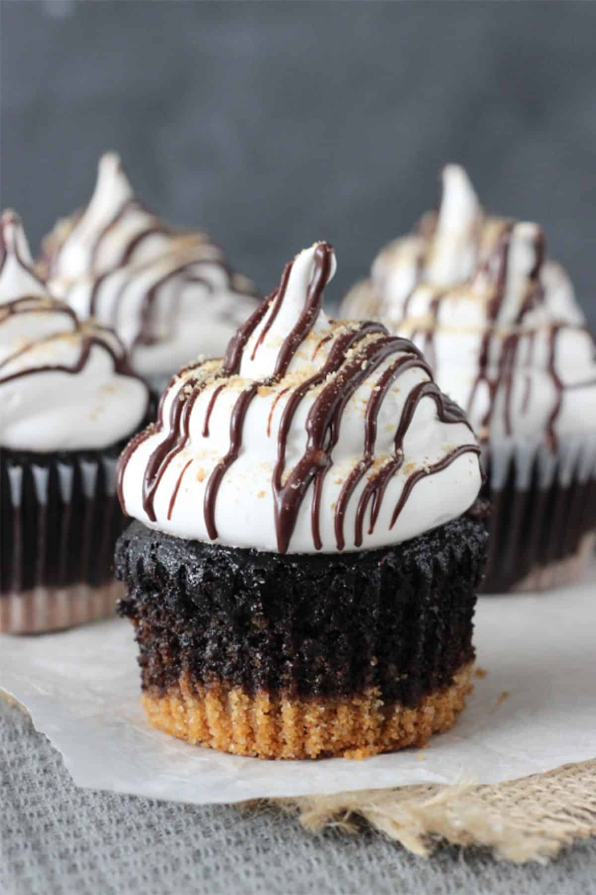 Close up of a S'mores Cupcake on a piece of parchment with more cupcakes in the background.