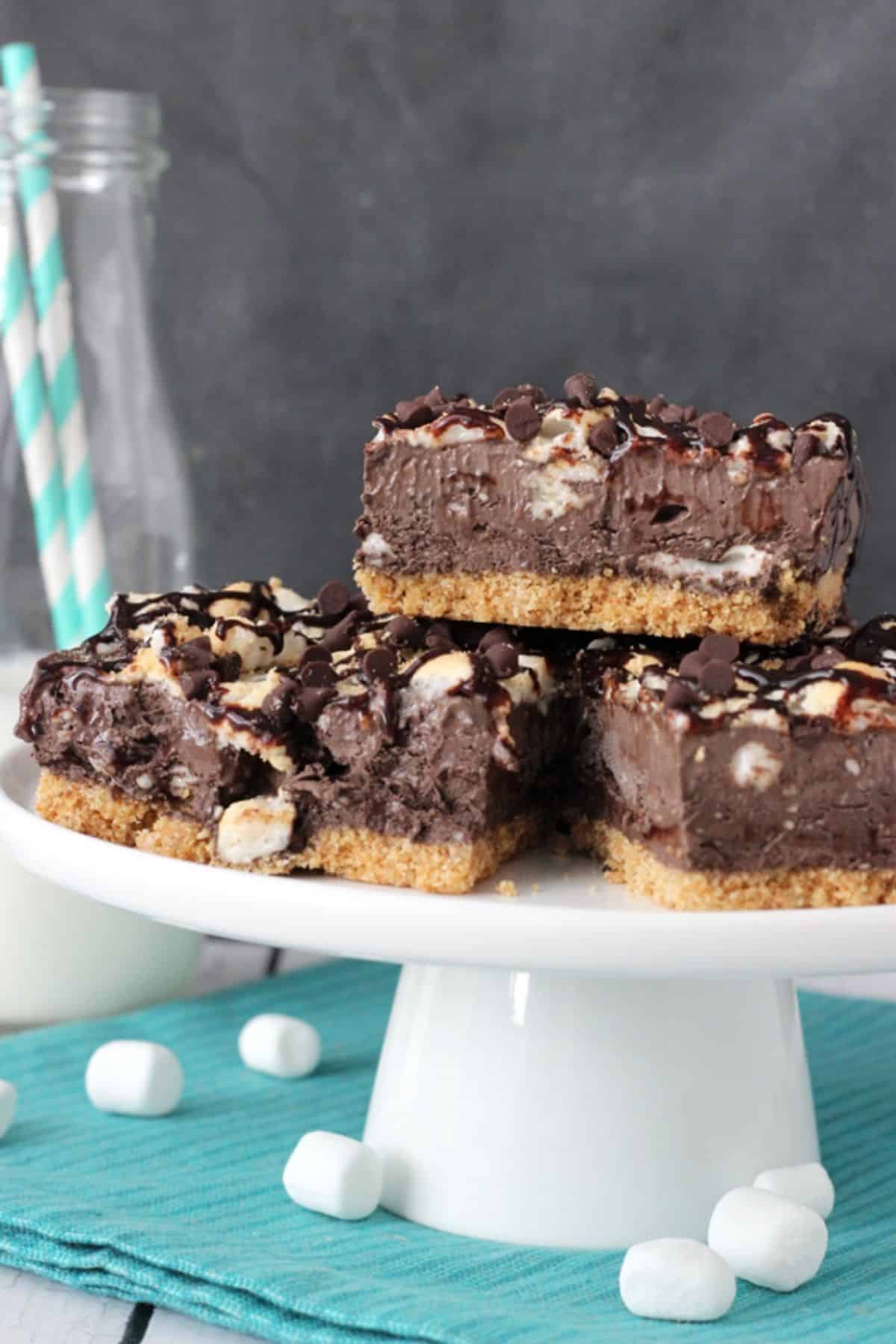 Three slices of s'mores ice cream bars on a white cake stand.