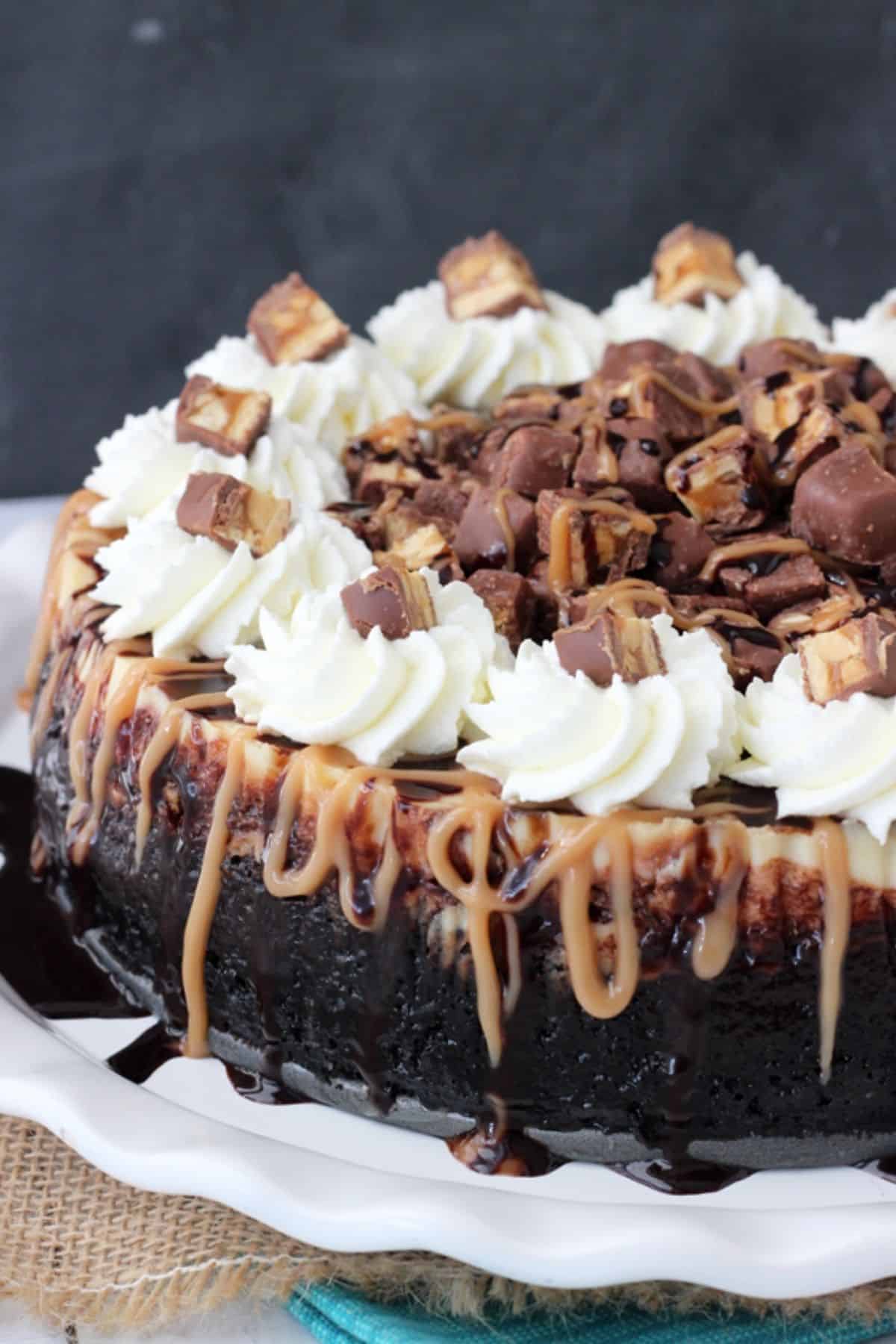 Close up of the side and top of a Snickers cheesecake on a white cake plate.