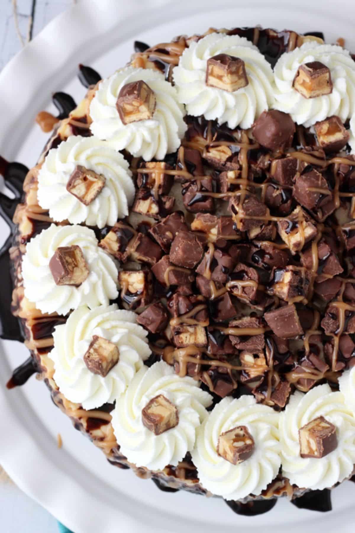 The top of a Snickers cheesecake on a white cake plate.